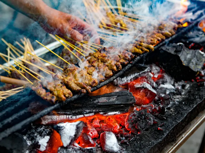 Brutzelnde Satay-Spieße werden von Hand über glühender Holzkohle auf einem Streetfood-Markt in Penang, Malaysia, gewendet.