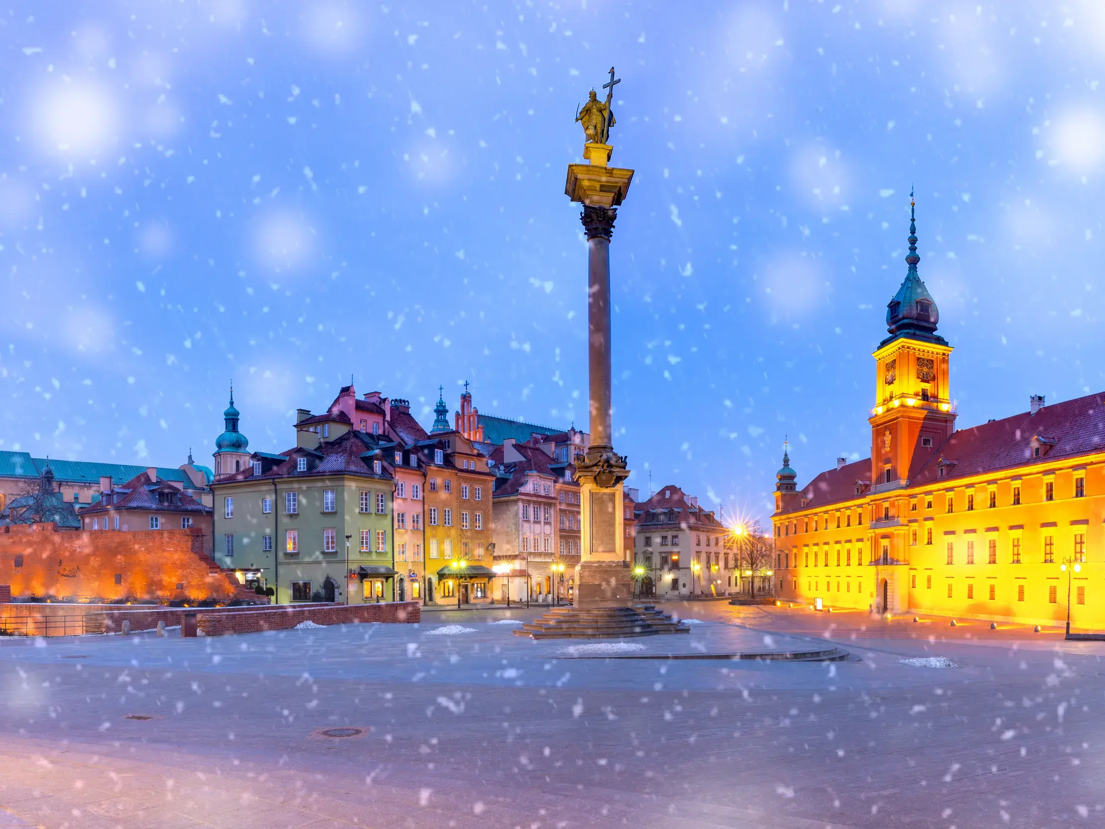 Der verschneite Schlossplatz in Warschau in der Dämmerung mit der Sigismundsäule und dem beleuchteten Königsschloss.