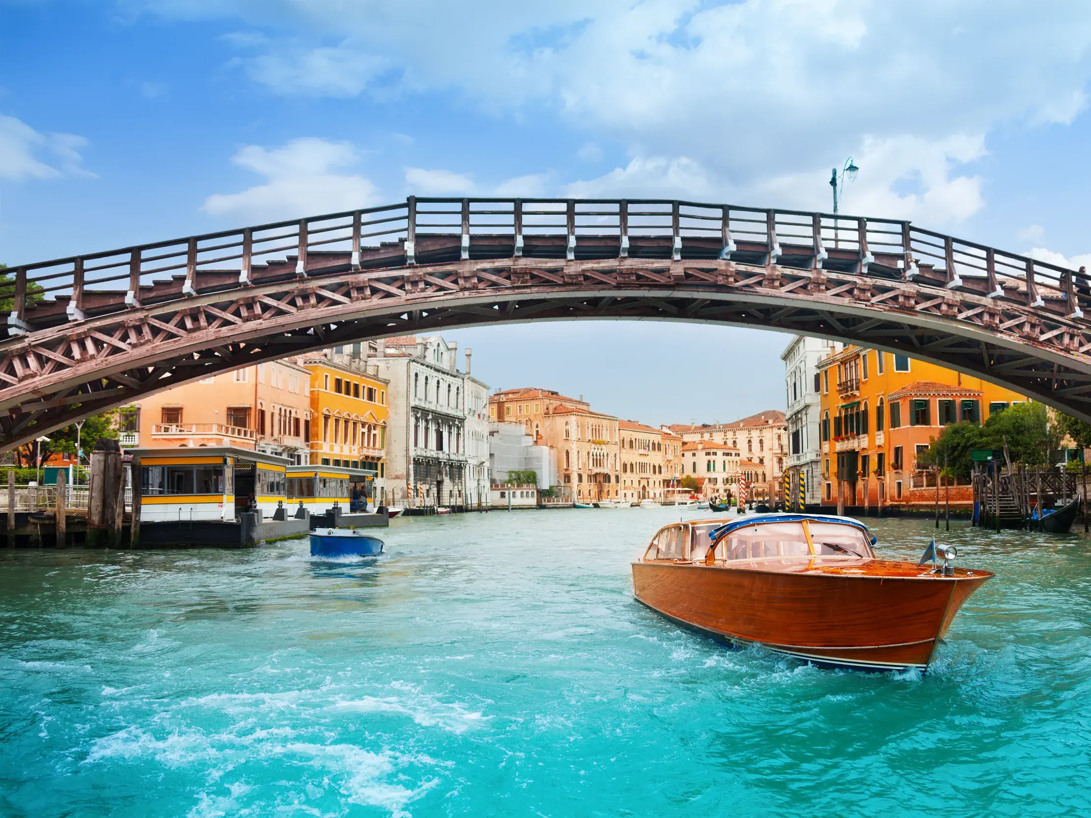 Ein hölzernes Wassertaxi auf dem Canal Grande in Venedig, umgeben von historischen Palästen unter einer eleganten Fußgängerbrücke.