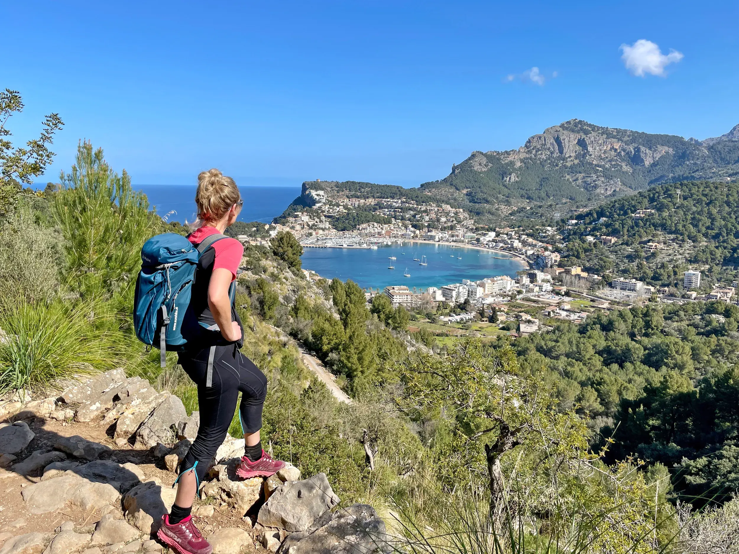 Eine Wanderin auf einem Felsenpfad in der Serra de Tramuntana mit Panoramablick auf die Bucht von Port de Sóller.