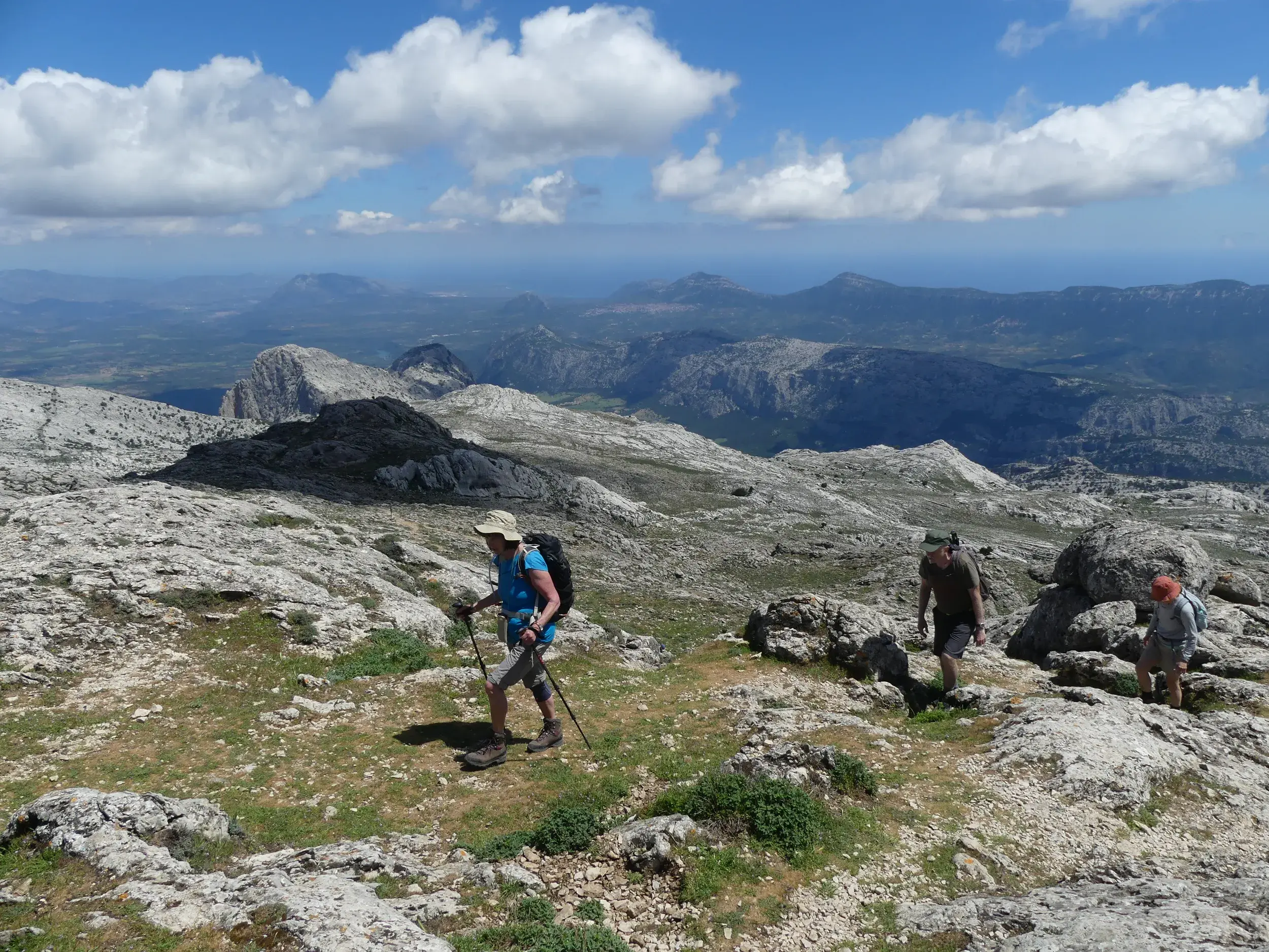 Drei Wanderer erkunden auf einem schmalen Pfad die felsige Bergwelt des Supramonte auf Sardinien mit weitem Ausblick.
