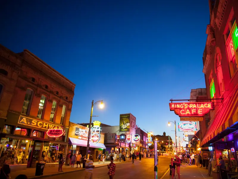 Die belebte Beale Street in Memphis in der Abenddämmerung, gesäumt von historischen Gebäuden und leuchtenden Neonschildern.