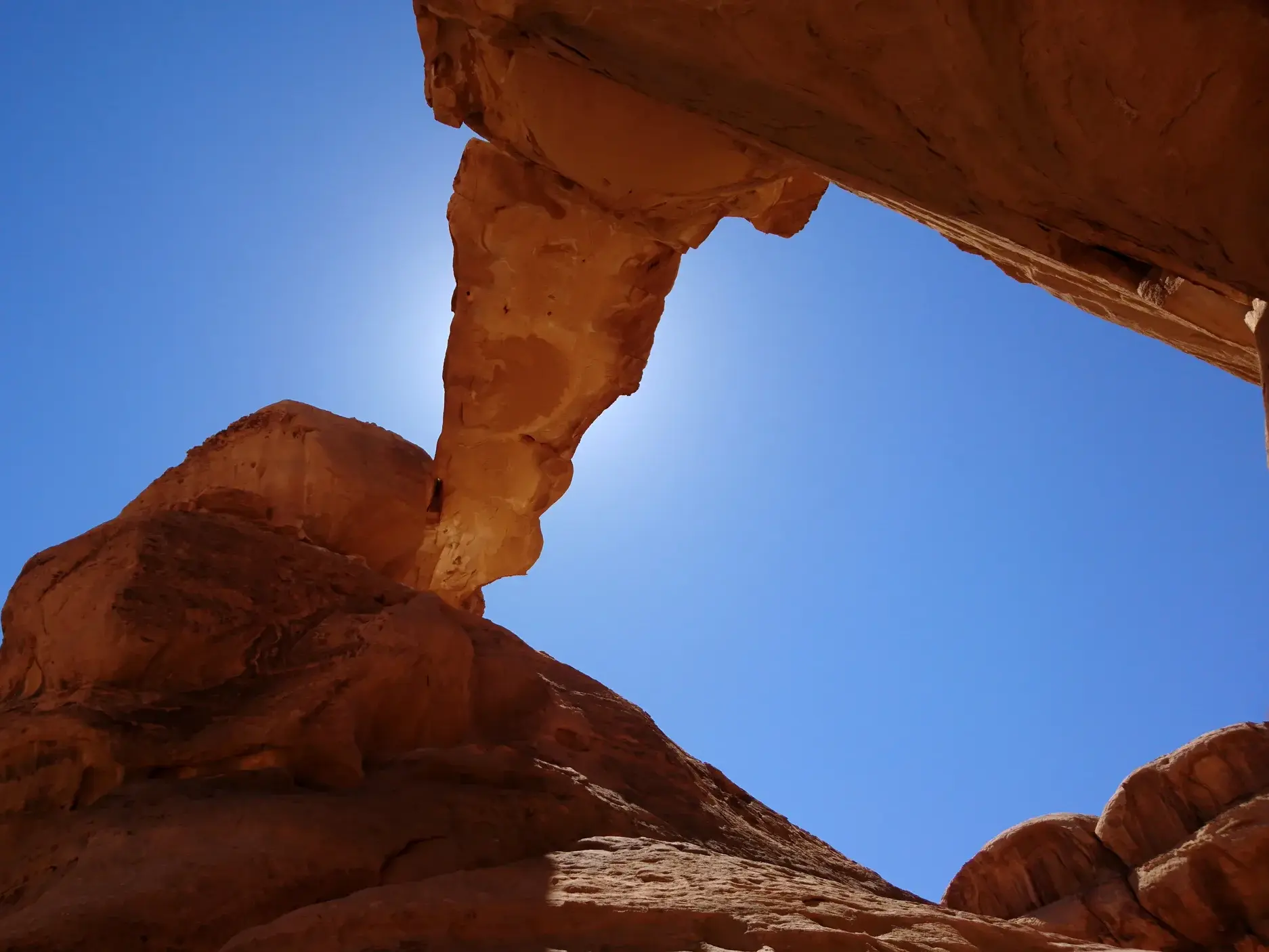 Eine natürliche Felsbrücke aus rotem Sandstein im Wadi Rum, Jordanien, im strahlenden Gegenlicht der Wüstensonne.
