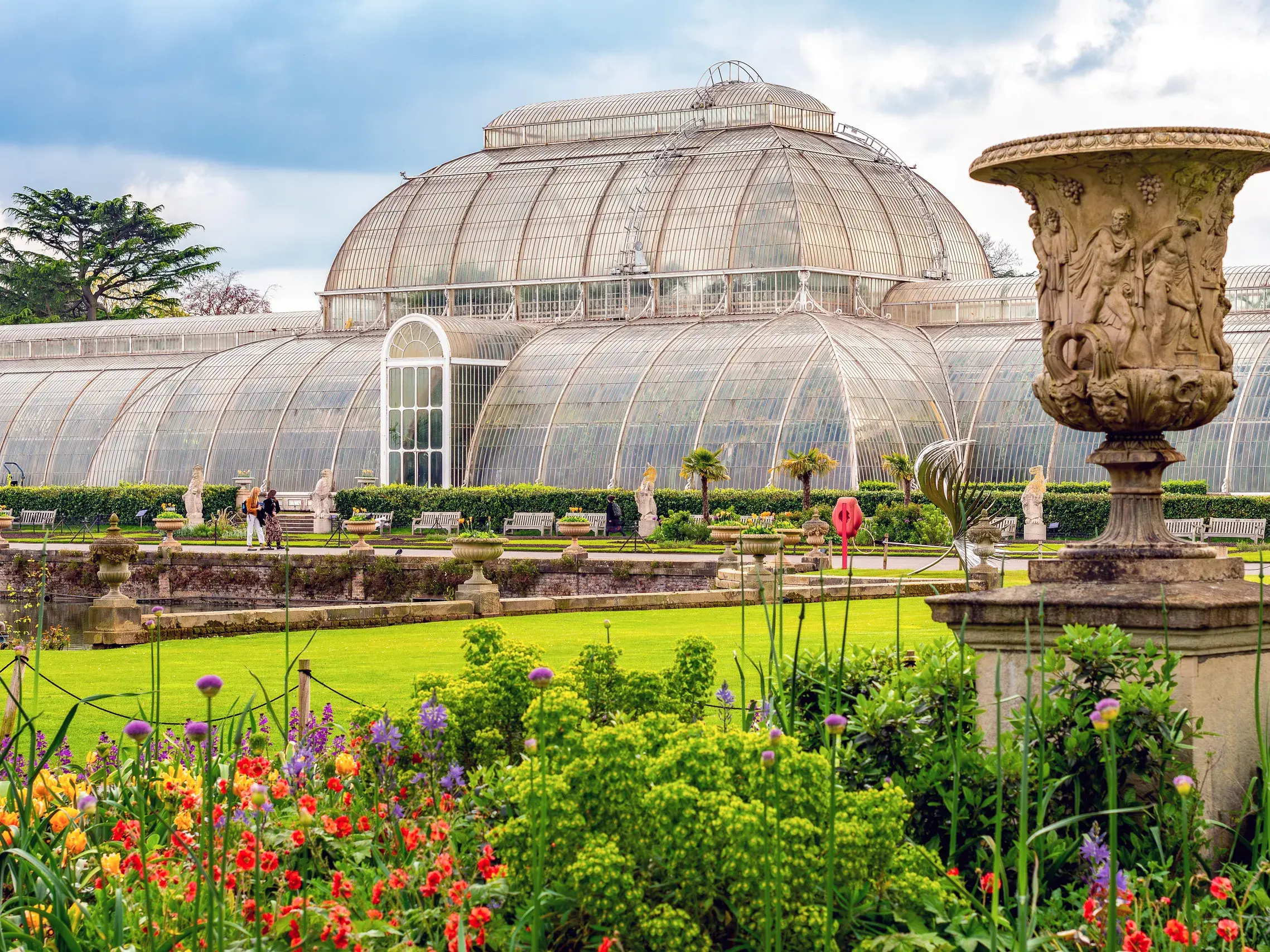 Historisches Palmenhaus aus Glas hinter bunten Blumenbeeten in den Kew Gardens bei London