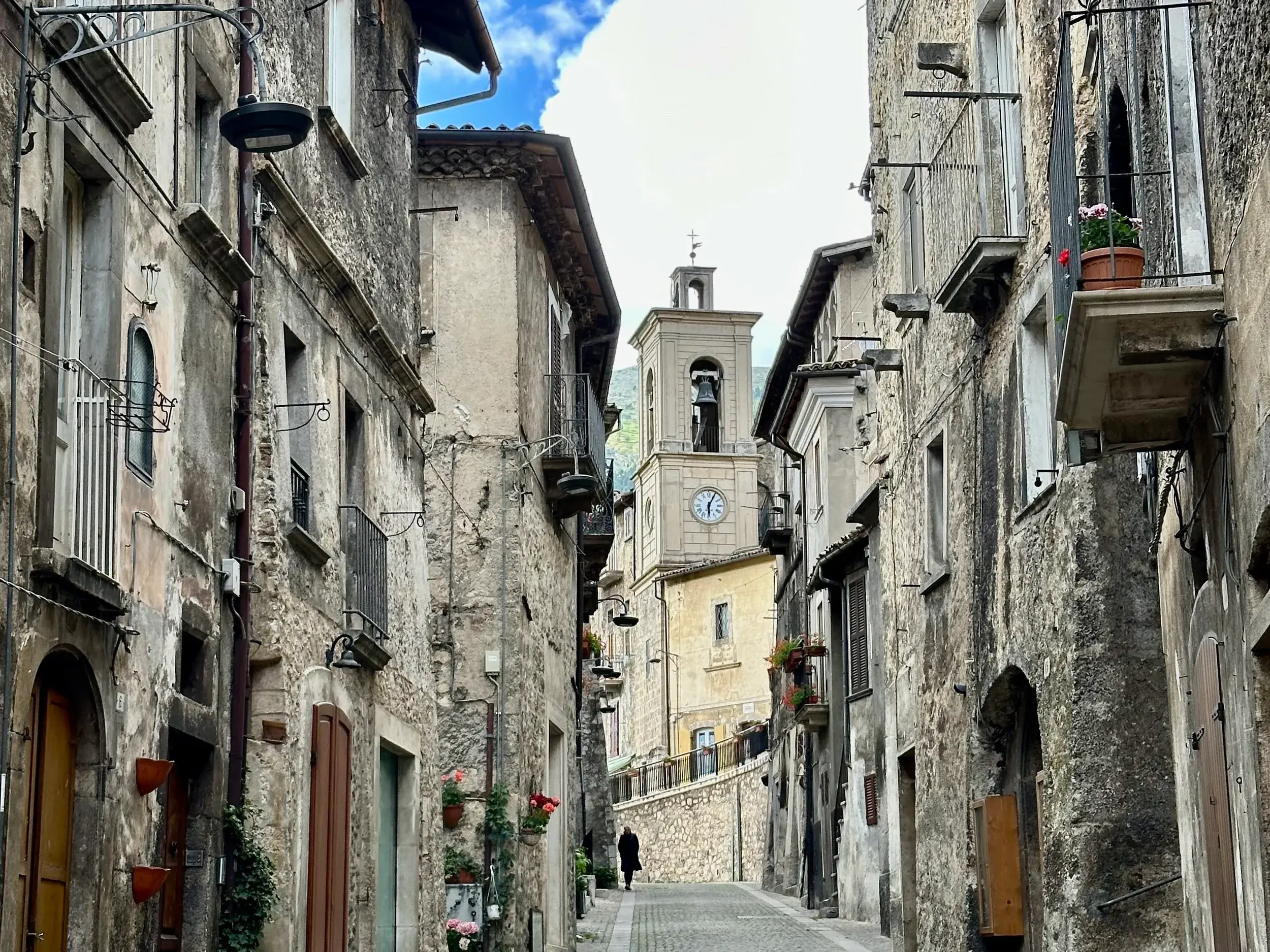 Historische Gasse im Bergdorf Scanno mit alten Steinfassaden, Balkonen und Blick auf einen Glockenturm in den Abruzzen.