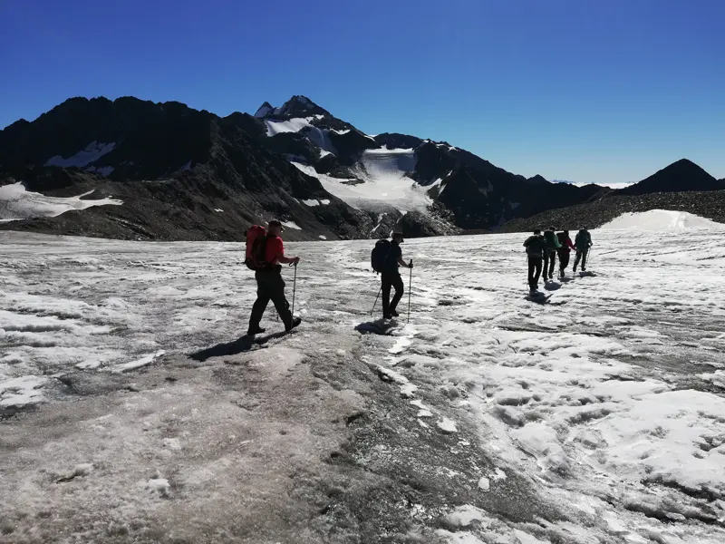 Bergwanderführer leitet eine kleine Reisegruppe über einen weiten Gletscher in den Stubaier Alpen bei strahlendem Sonnenschein.