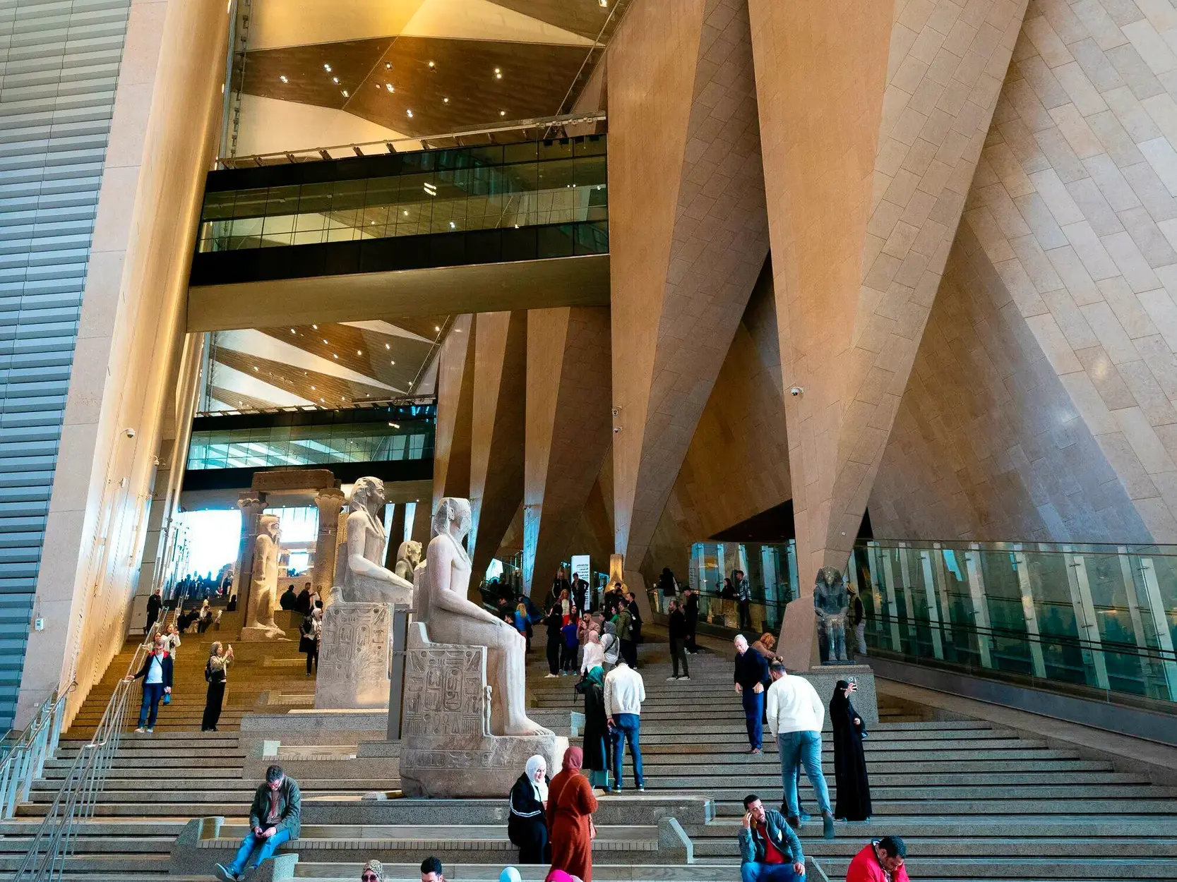 Besucher auf der großen Treppe mit antiken Statuen im Grand Egyptian Museum in Gizeh