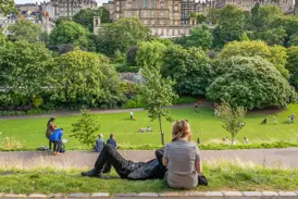 Menschen genießen einen sonnigen Tag in einem Park mit Blick auf die beeindruckende Architektur der Altstadt von Edinburgh.