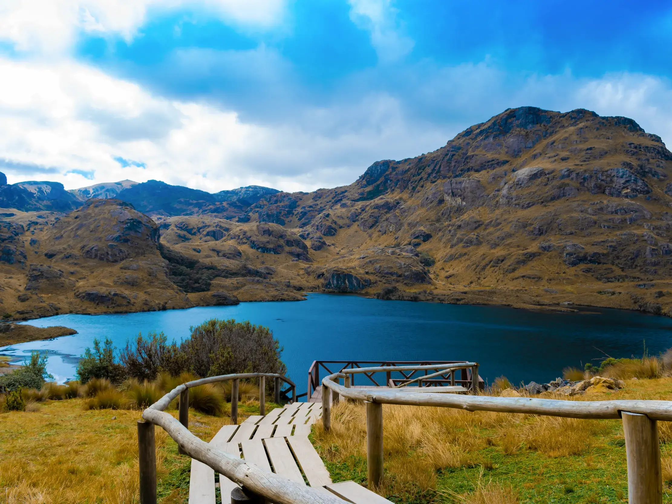 Ein Holzsteg führt hinunter zur blauen Lagune La Toreadora im Cajas-Nationalpark während einer Rundreise in Ecuador.
