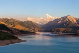 Der türkise Charvak-Stausee in Usbekistan, eingerahmt von den Gipfeln des Tien Shan-Gebirges im warmen Abendlicht.