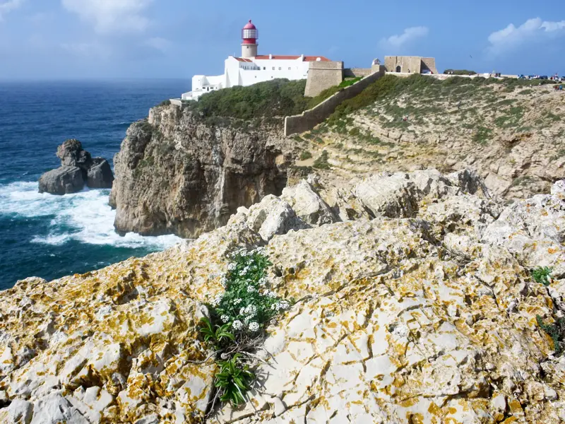 Felsige Steilküste mit dem Leuchtturm des Cabo de São Vicente über dem tosenden Atlantik an der Costa Vicentina.