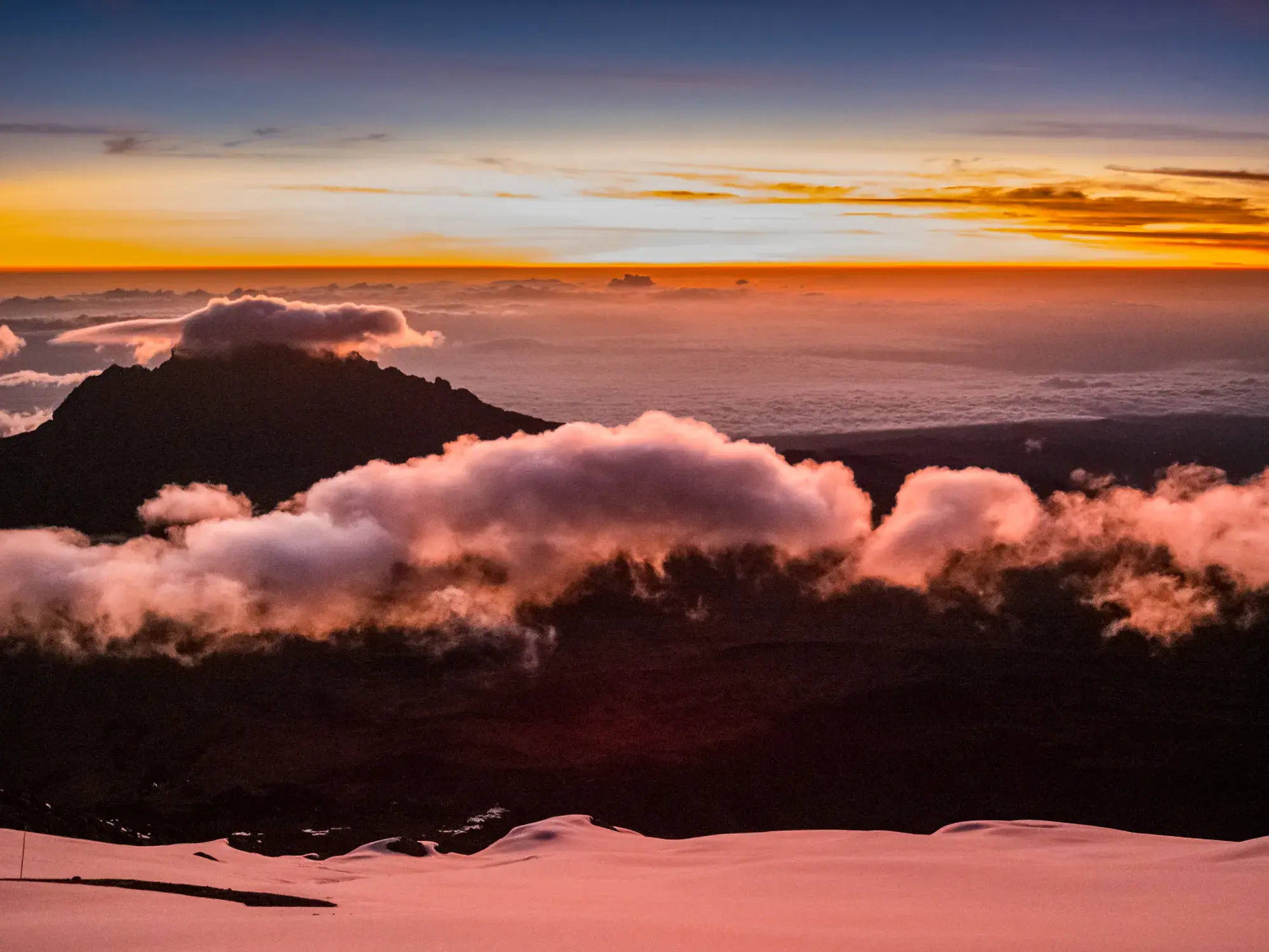 Faszinierender Sonnenaufgang beim Kilimanjaro-Trekking mit Blick vom Gipfel über Wolken und schneebedeckte Hänge in Tansania.