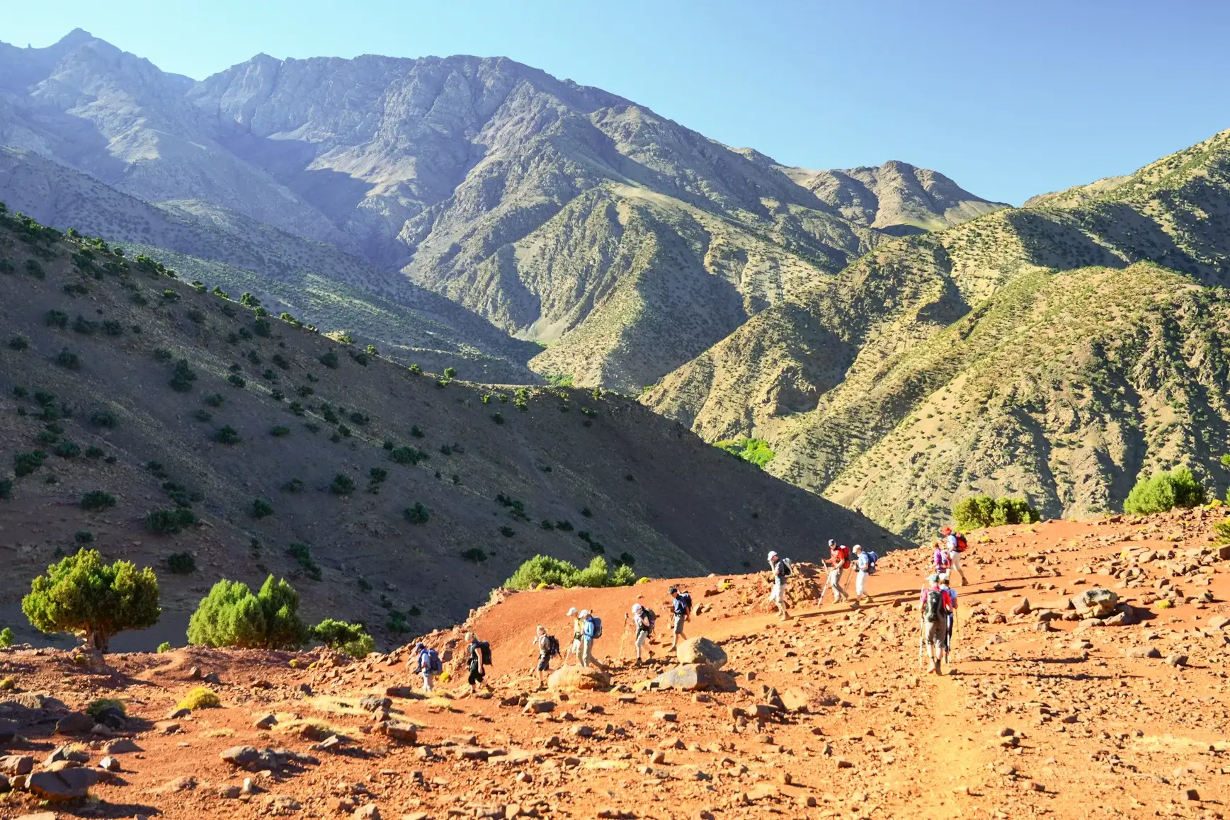 Eine Hauser-Wandergruppe beim Trekking auf einem roten Gebirgspfad im Hohen Atlas mit weiter Aussicht auf die Gipfelkette.