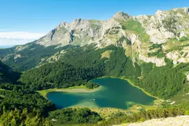 Panoramablick beim Trekking auf einen türkisen, herzförmigen Bergsee, umrahmt von dichten Wäldern und einer schroffen Gebirgskette.