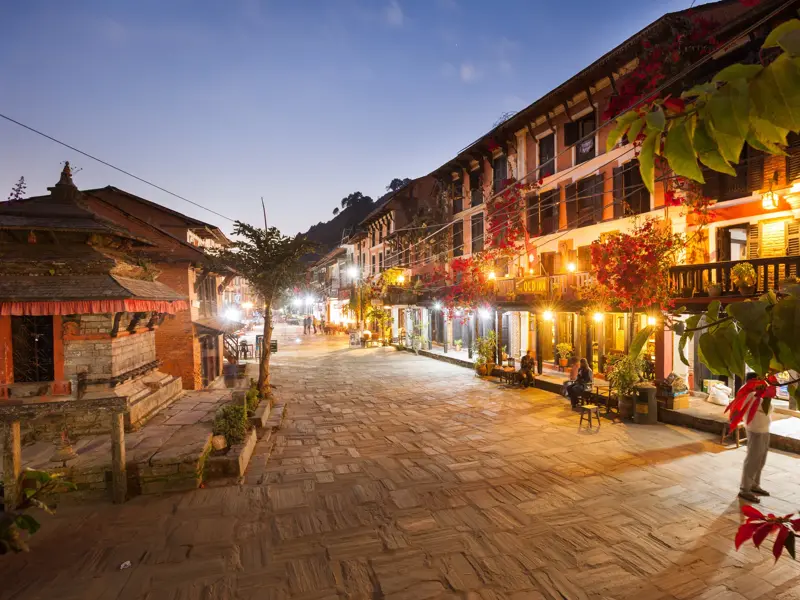 Autofreie Gasse im historischen Bergdorf Bandipur in Nepal bei Dämmerung, gesäumt von beleuchteten Newari-Häusern.