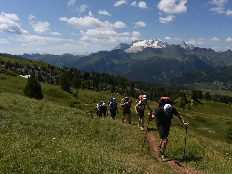 Eine Wandergruppe auf Trekkingtour über eine grüne Almwiese in den Dolomiten mit Panoramablick auf die Marmolata.