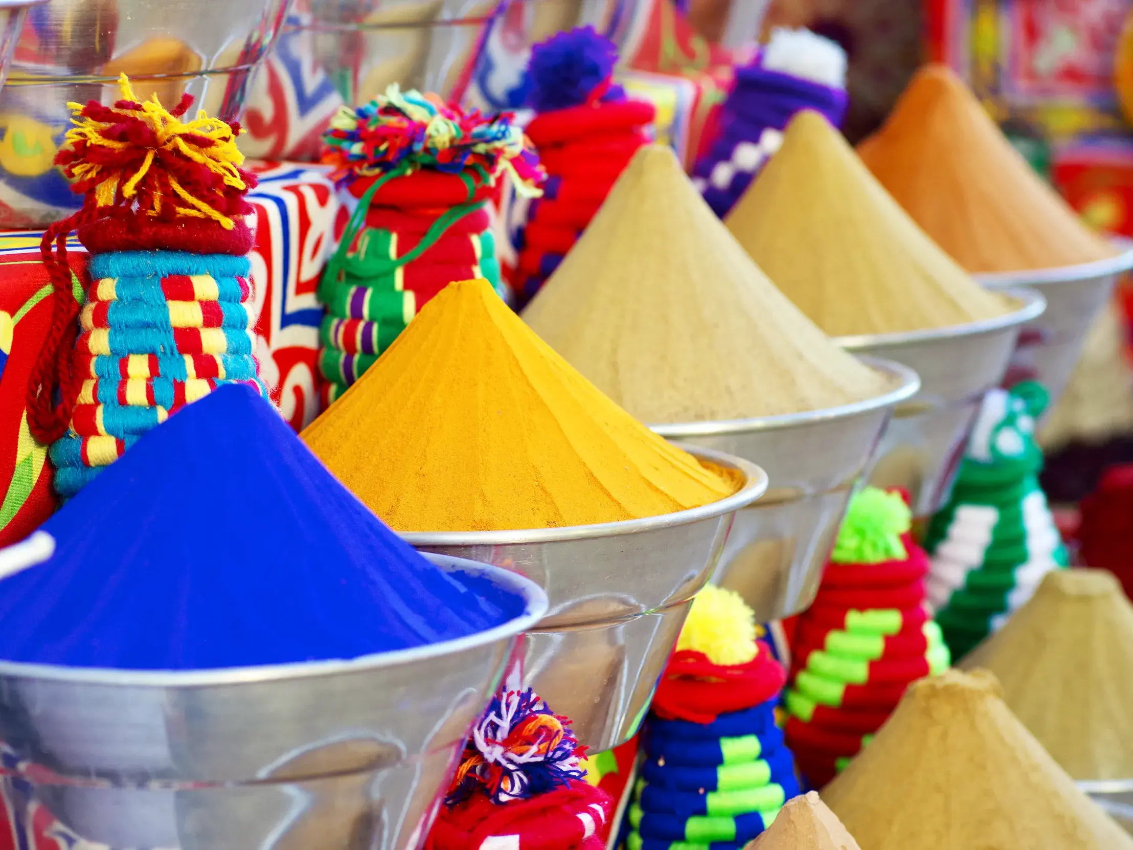 Pyramidenförmig aufgetürmte, farbenfrohe Gewürze wie Kurkuma und Indigo in Metallschalen auf einem Basar in Kairo.