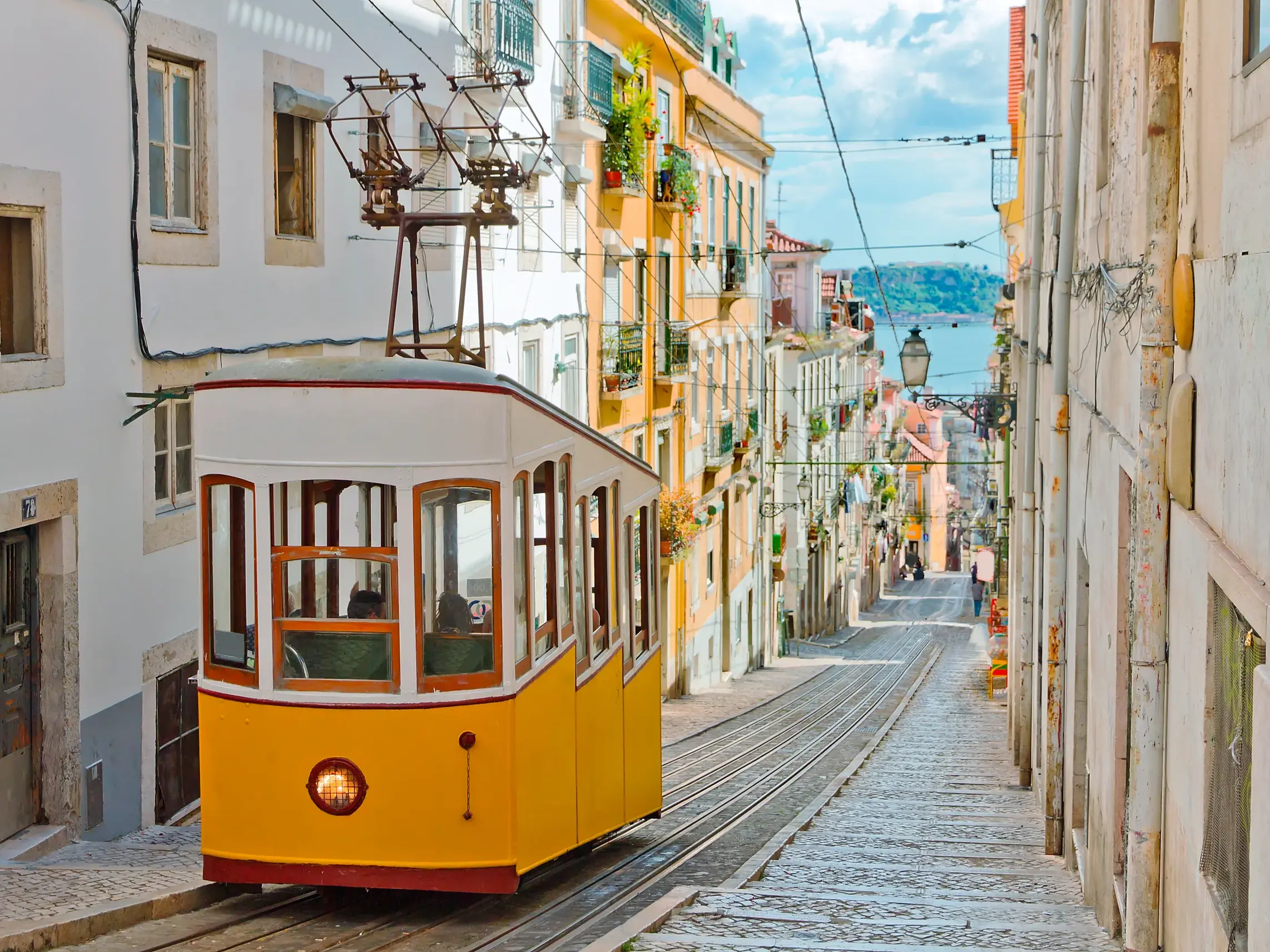 Eine ikonische gelbe Straßenbahn fährt durch eine enge Kopfsteinpflaster-Gasse in der Altstadt von Lissabon.