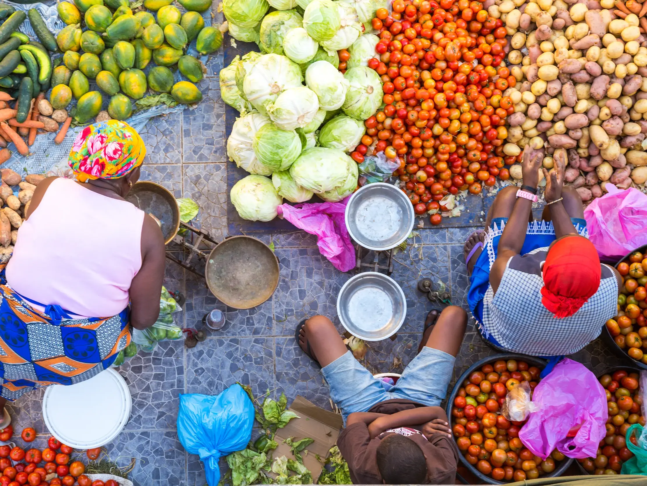 Vogelperspektive auf einen bunten Markt auf den Kapverden: Händlerinnen sitzen zwischen frischen Tomaten, Kohl und Papayas.