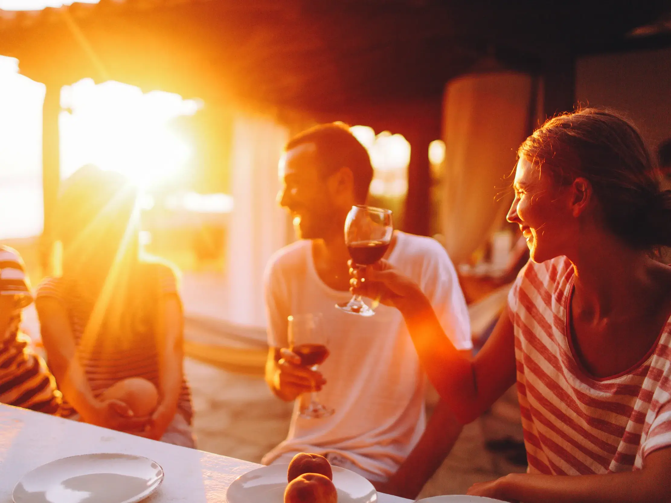 Eine Kleingruppenreise in Indonesien: Gäste genießen lachend ein gemeinsames Abendessen im warmen Licht des Sonnenuntergangs.