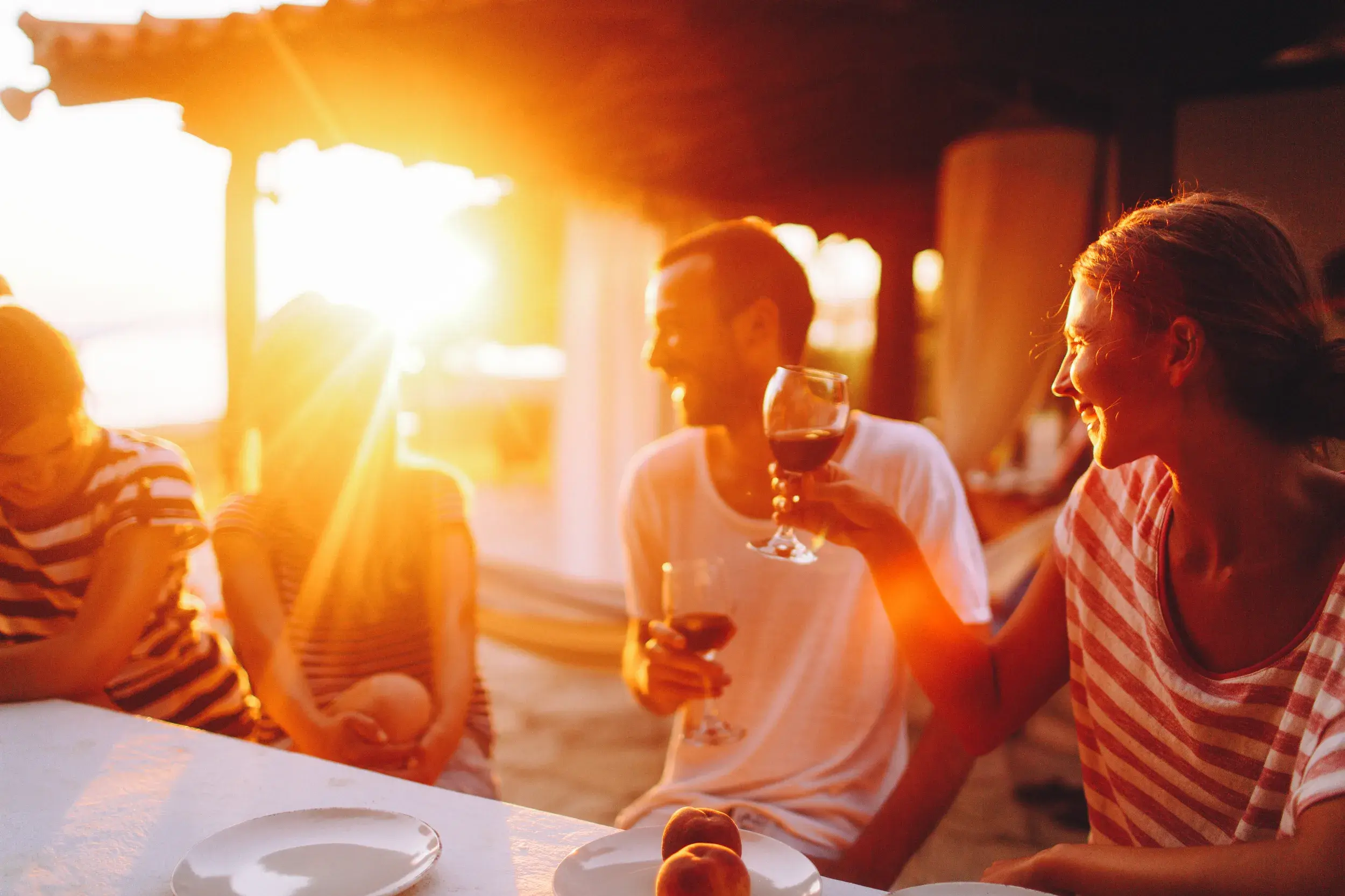 Eine Kleingruppenreise in Indonesien: Gäste genießen lachend ein gemeinsames Abendessen im warmen Licht des Sonnenuntergangs.