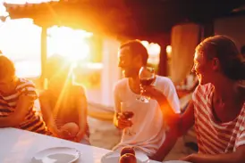 Eine Kleingruppenreise in Indonesien: Gäste genießen lachend ein gemeinsames Abendessen im warmen Licht des Sonnenuntergangs.