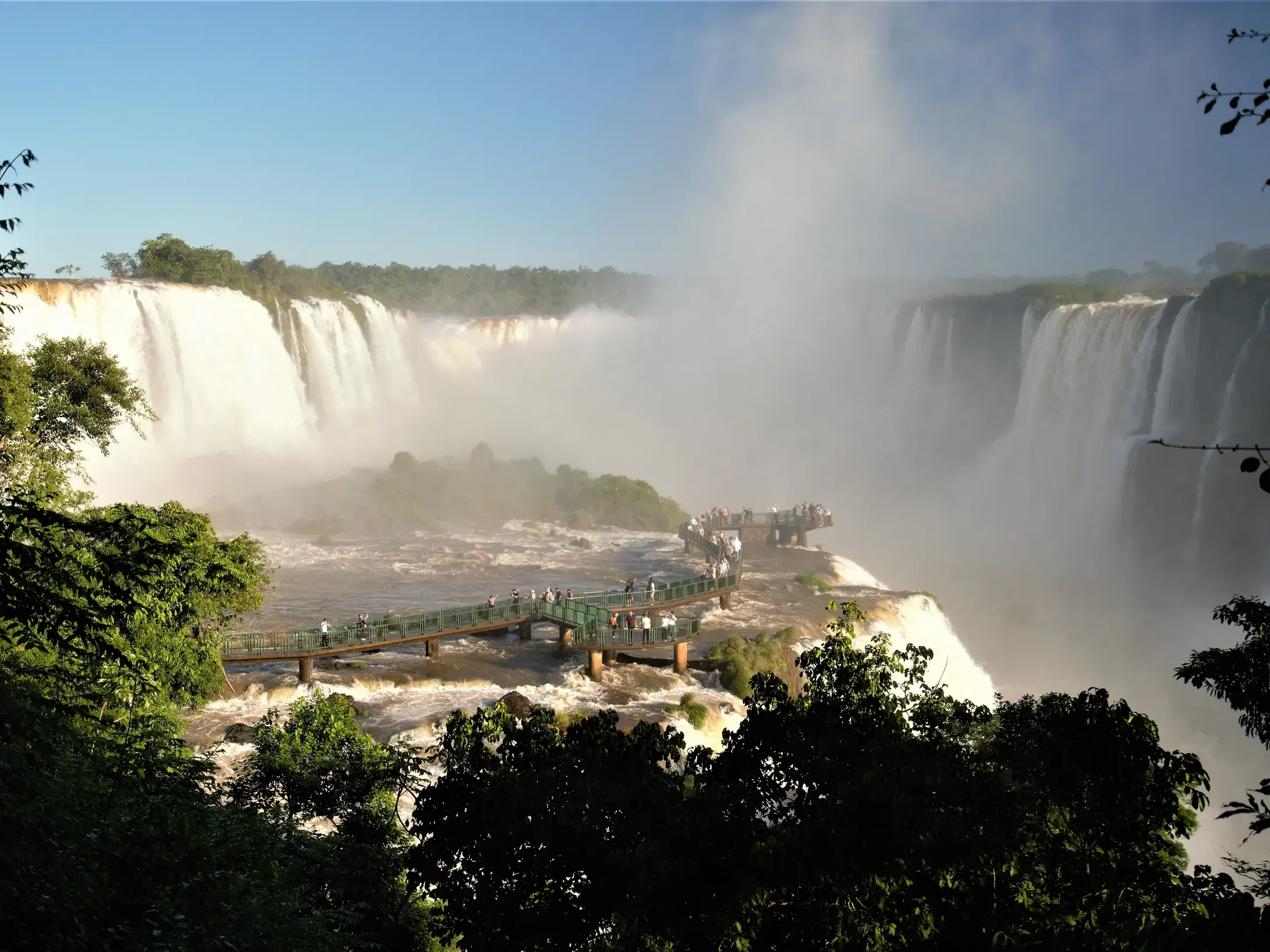 Eine Reisegruppe steht auf einer Aussichtsplattform nahe an gewaltigen, nebelverhangenen Wasserfällen in Brasilien.