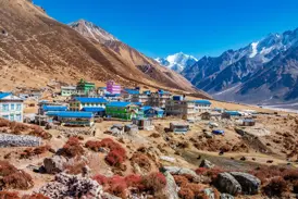 Das Bergdorf Kyanjin Gompa im Langtang-Nationalpark mit bunten Häusern vor der Kulisse schneebedeckter Himalaya-Gipfel.
