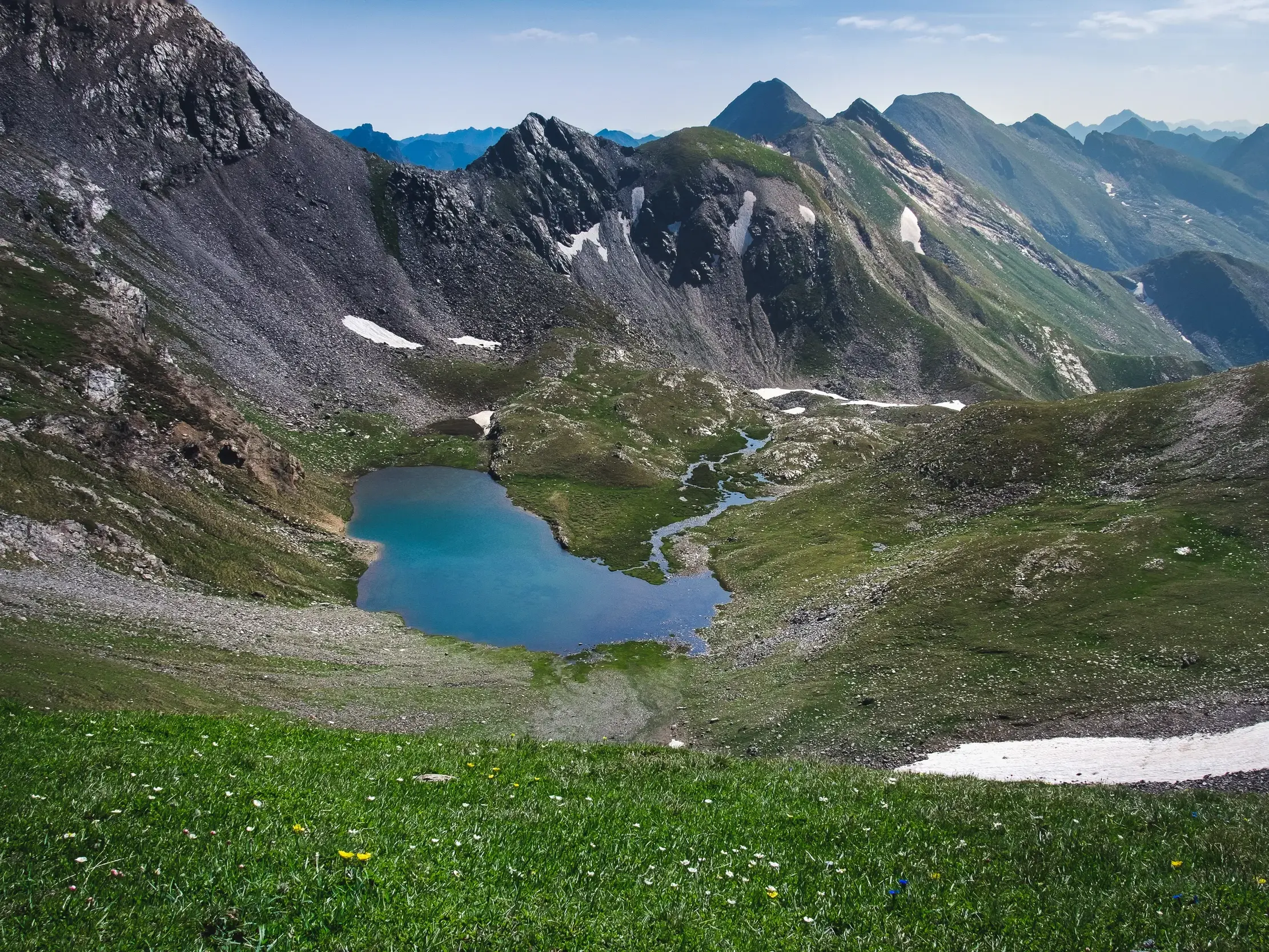 Türkisblauer Karsee in einem Hochtal der andorranischen Pyrenäen, umgeben von schroffen Gipfeln und grünen Almwiesen.