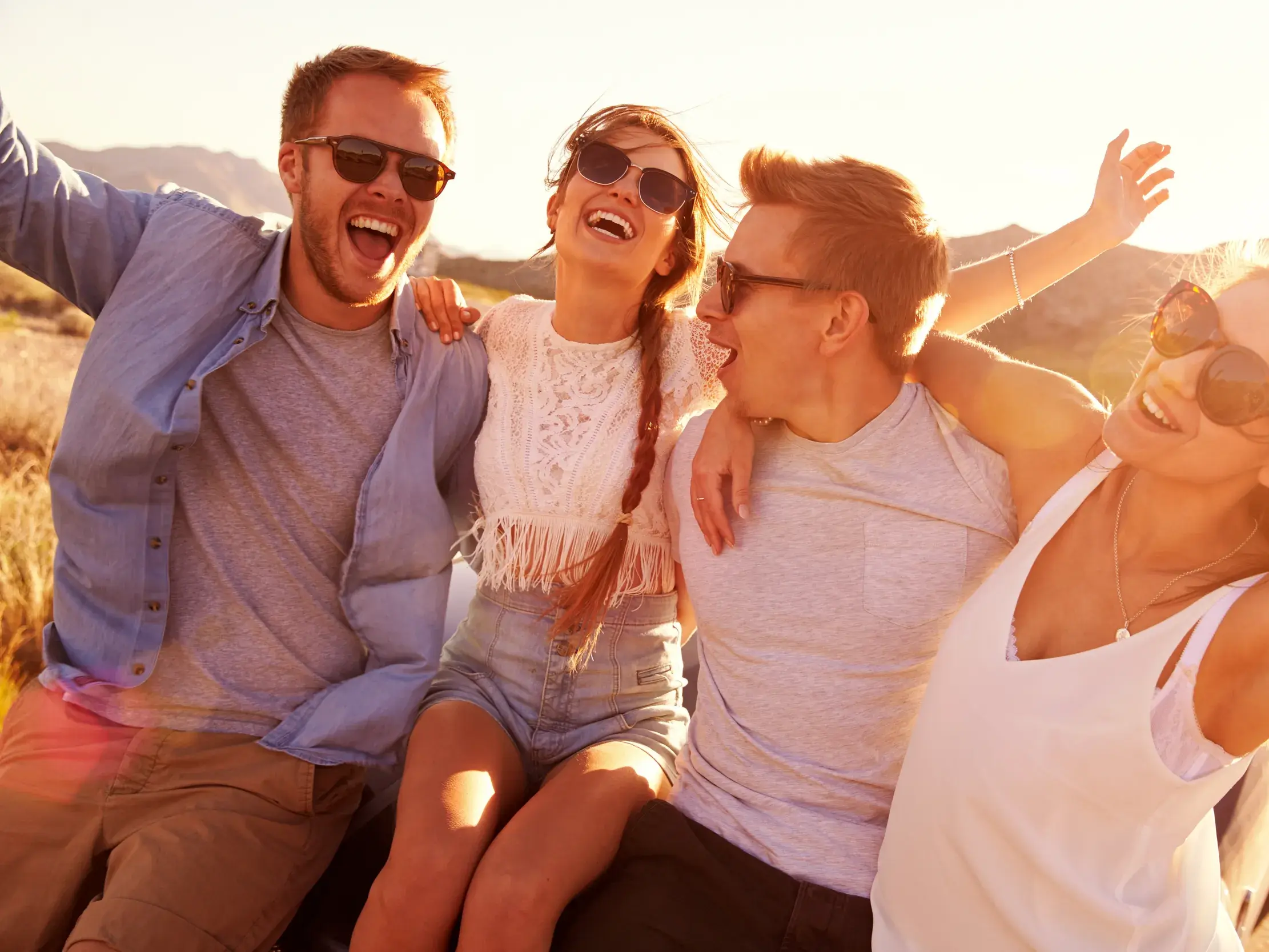 Vier junge Reisende einer Kleingruppe lachen und umarmen sich ausgelassen während eines sonnigen Stopps auf ihrer Rundreise auf Bali.