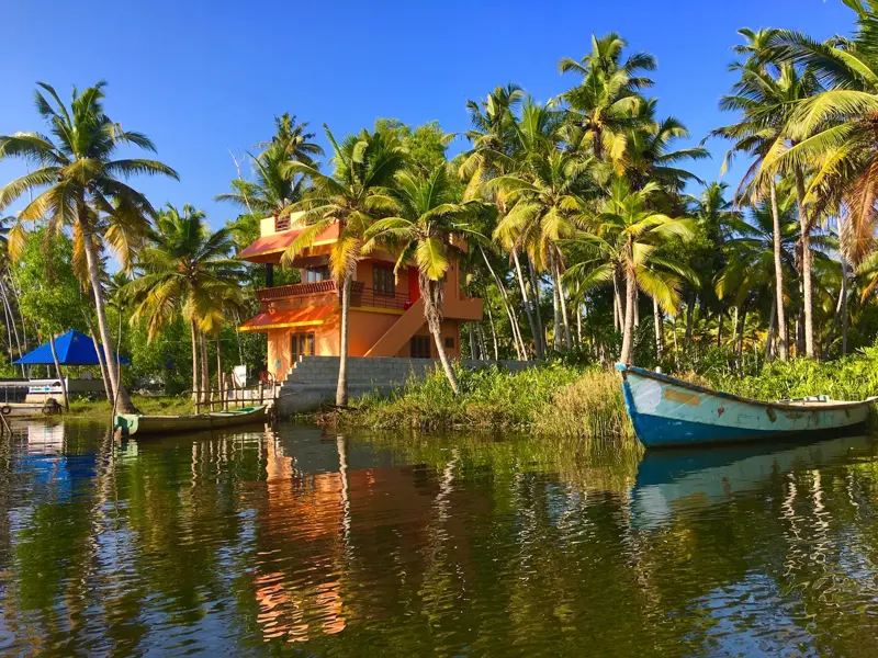 Tropisches Haus an einem Kanal der Kerala Backwaters, umgeben von Kokospalmen, die sich auf der ruhigen Wasseroberfläche spiegeln.