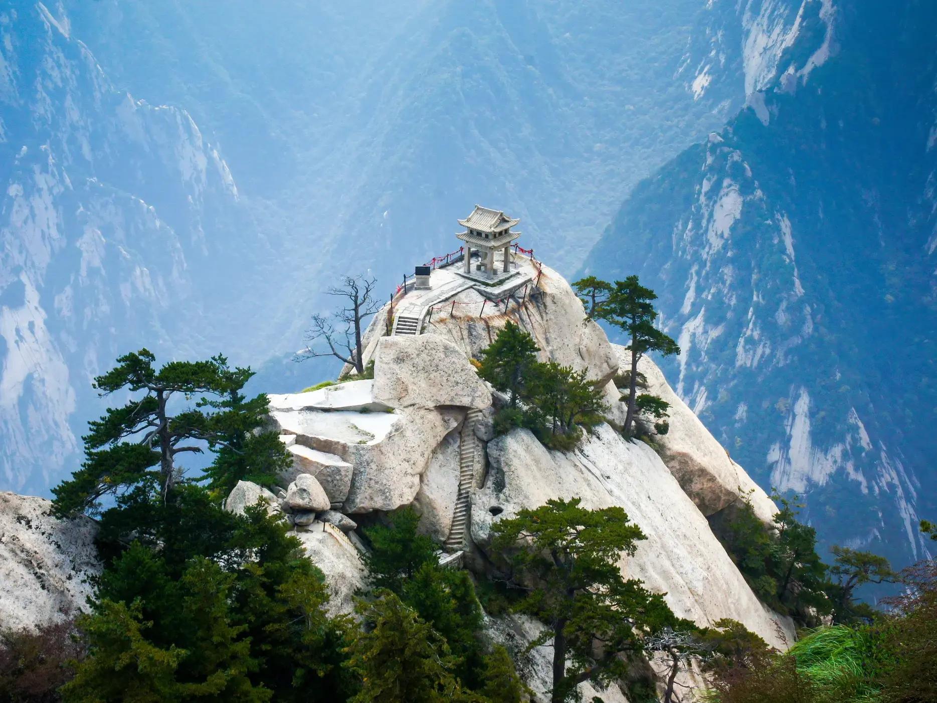 Ein traditioneller Pavillon auf einem steilen Felsgipfel des Hua Shan, umgeben von Kiefern und nebliger Berglandschaft Chinas.