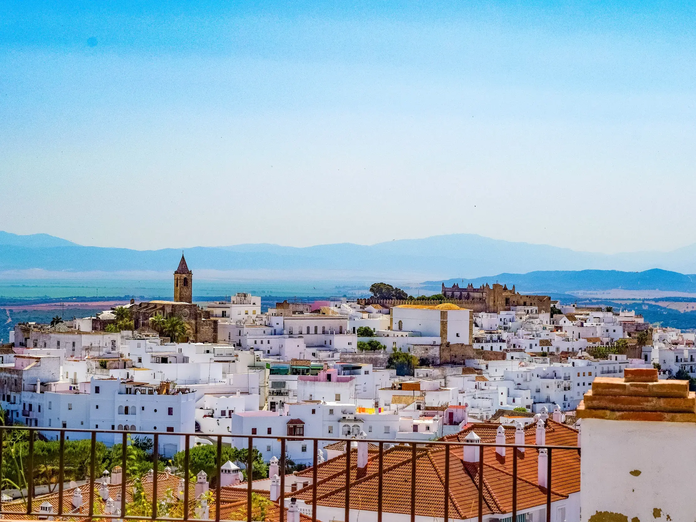 Sonniger Panoramablick auf das weiße Dorf Vejer de la Frontera in Andalusien, im Hintergrund eine weite Ebene und Berge.