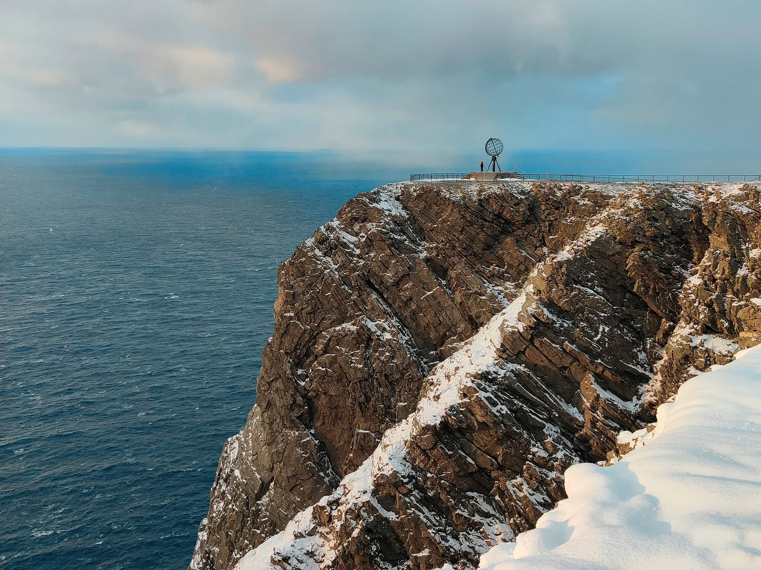 Die schneebedeckten Klippen des Nordkaps in Norwegen mit dem Globusmonument und Blick auf das weite Polarmeer im Winter.