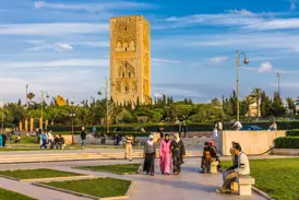 Drei Frauen in traditioneller Kleidung spazieren an einem sonnigen Tag durch den Park vor dem historischen Hassan-Turm in Rabat.