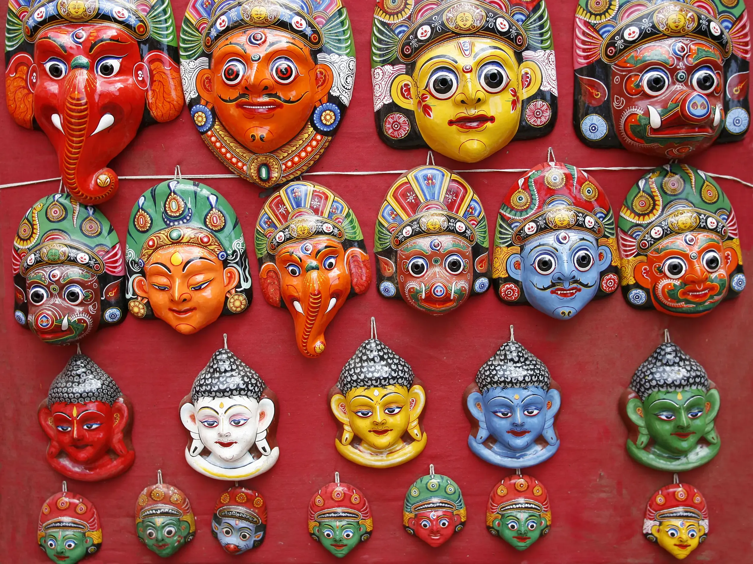 Vielfalt nepalesischen Kunsthandwerks: Bunte, handgeschnitzte Masken verschiedener Gottheiten hängen auf einem Markt in Nepal.