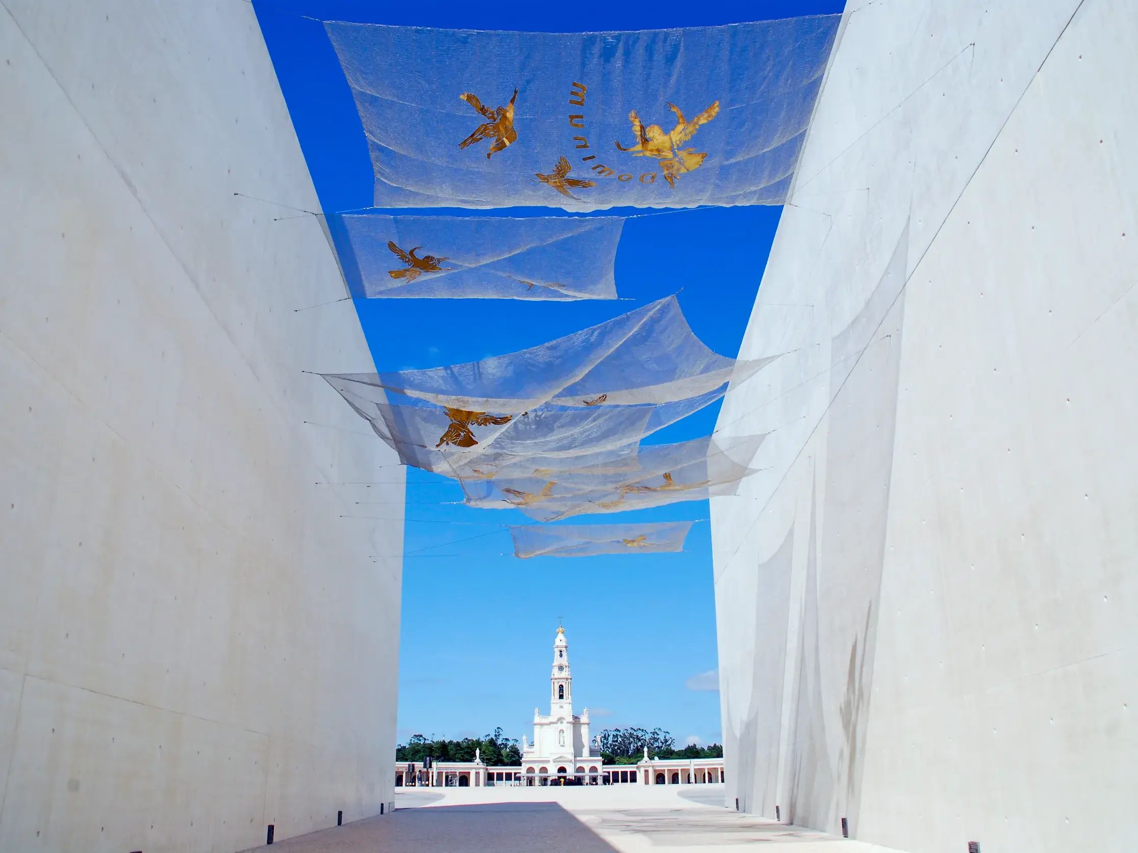 Weg zwischen hohen, weißen Mauern mit Bannern zum berühmten Wallfahrtsort Fatima und seiner Basilika in Portugal.