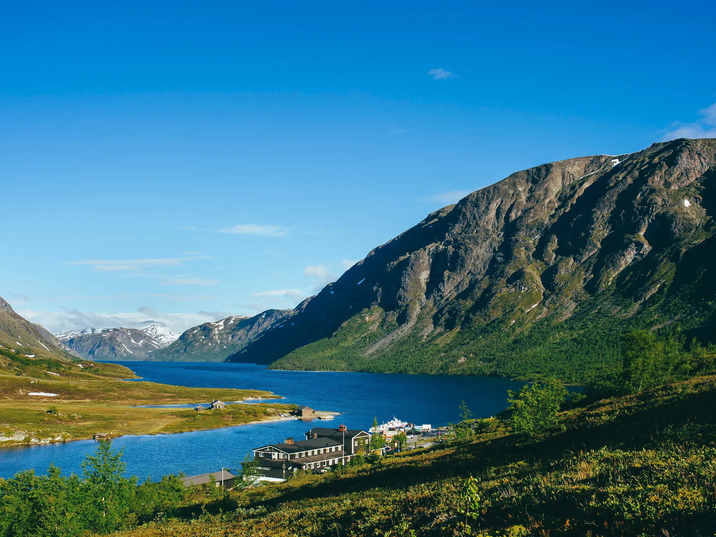Blick auf die malerische Berghütte Gjendesheim am Ufer des Gjende-Sees im Jotunheimen Nationalpark bei sonnigem Wetter.