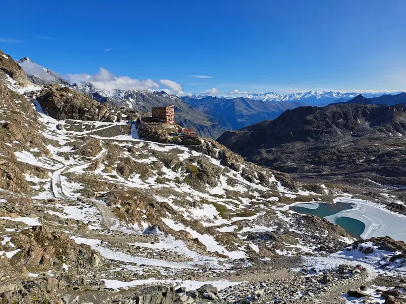 Panoramablick auf die Stettiner Hütte am Eisjöchl in der Texelgruppe mit teilgefrorenem Bergsee und Wanderweg in Südtirol.