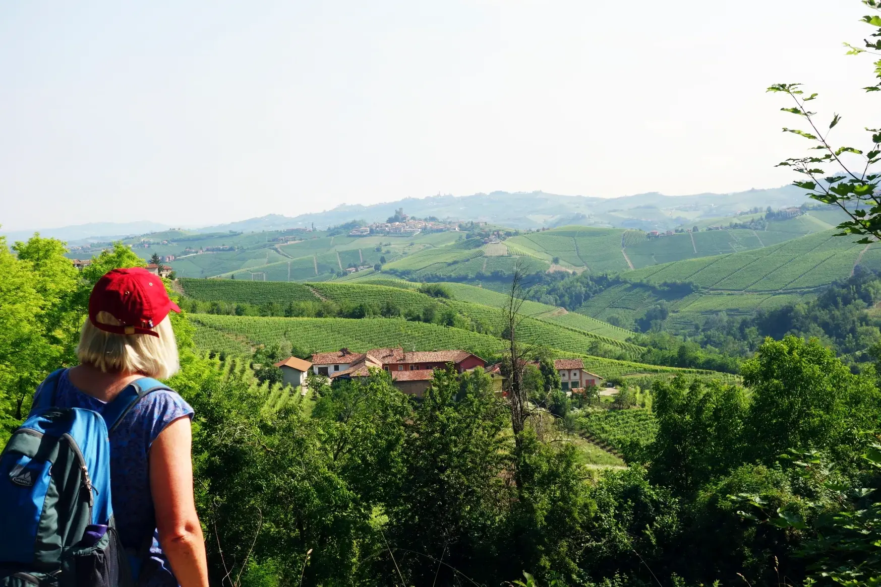 Wanderin mit Rucksack blickt vom "Balkon der Langhe" über die weiten Weinberge und Hügel des Barolo-Gebiets im Piemont.