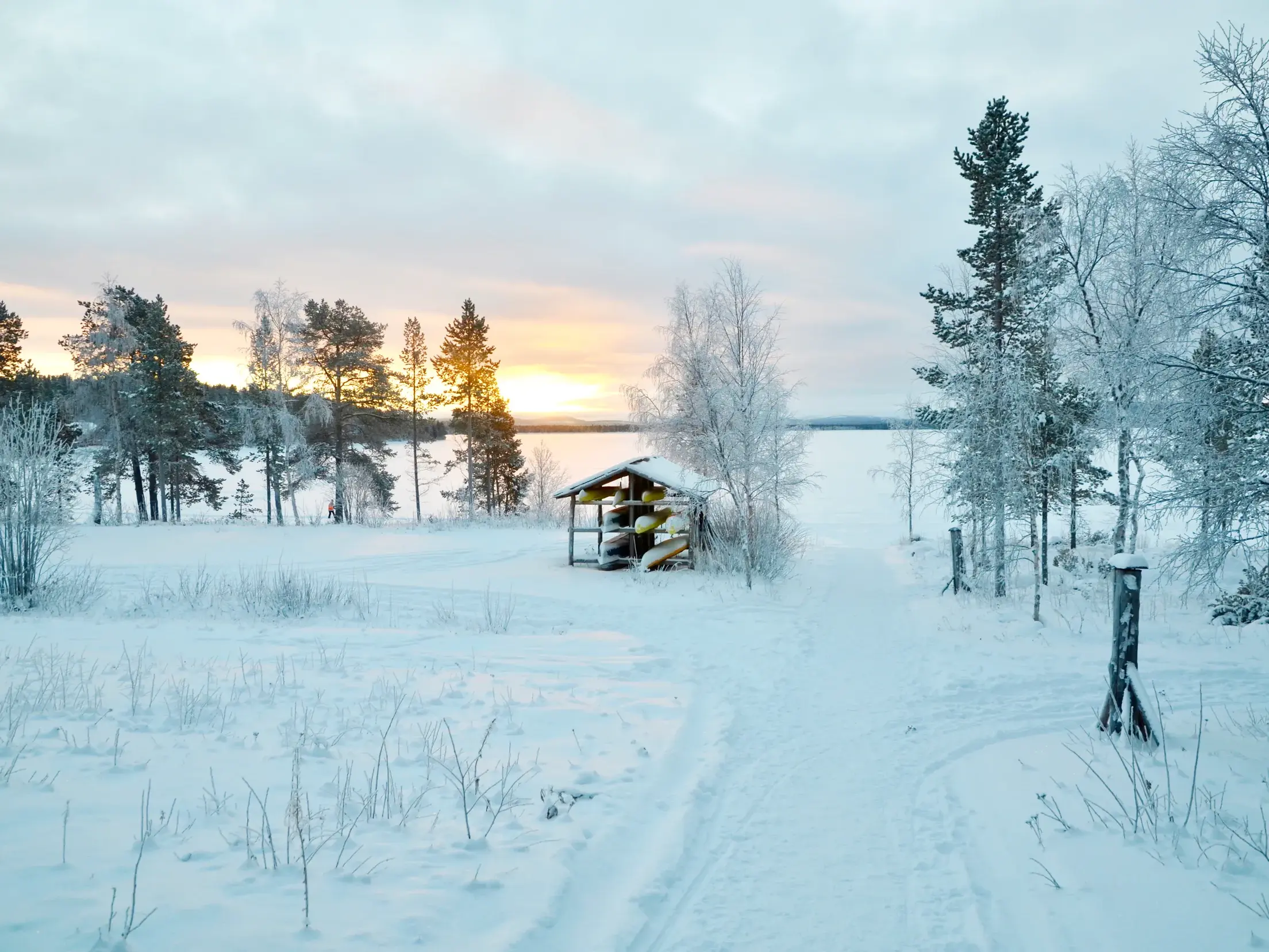 Verschneite Winterlandschaft mit Birken und Kanulager am Inari-See bei Sonnenuntergang in Lappland
