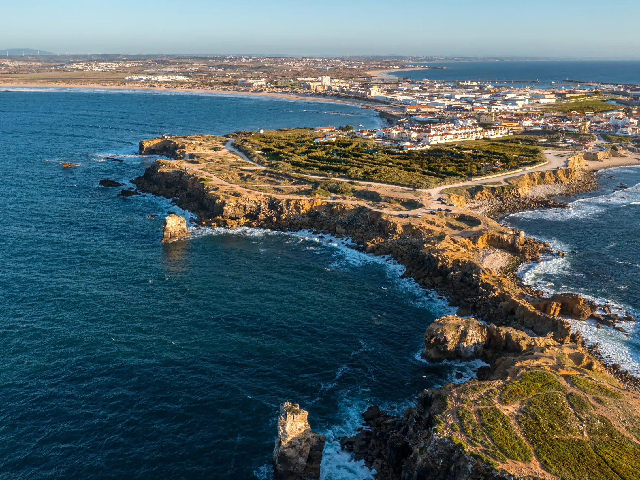 Die goldene Abendsonne beleuchtet die zerklüftete Felsküste und die Stadt Peniche an Portugals malerischer Atlantikküste.