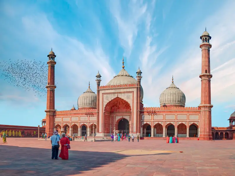 Zwei Reisende blicken auf die majestätische Jama Masjid Moschee aus rotem Sandstein in Delhi unter blauem Himmel.