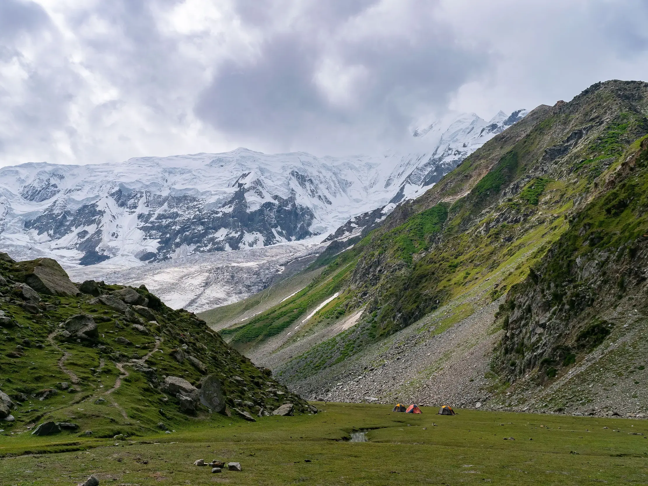 Zeltcamp im Rupal-Tal auf einer Trekkingreise mit Blick auf die riesige, schneebedeckte Rupalwand des Nanga Parbat.
