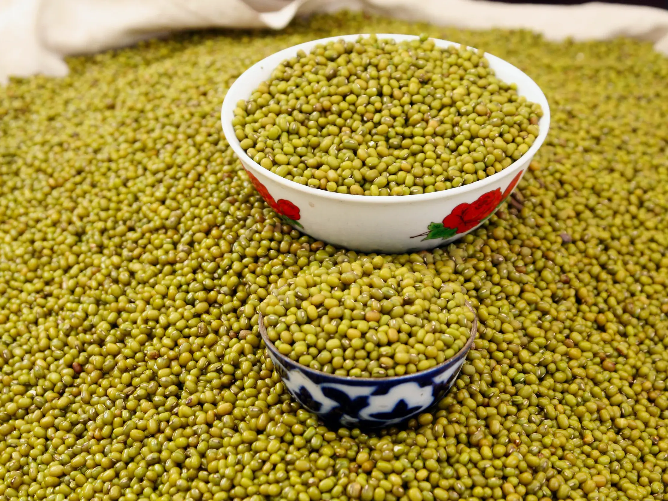 Grüne Mungobohnen werden in zwei traditionell verzierten Schalen auf einem belebten Basar in Usbekistan angeboten.