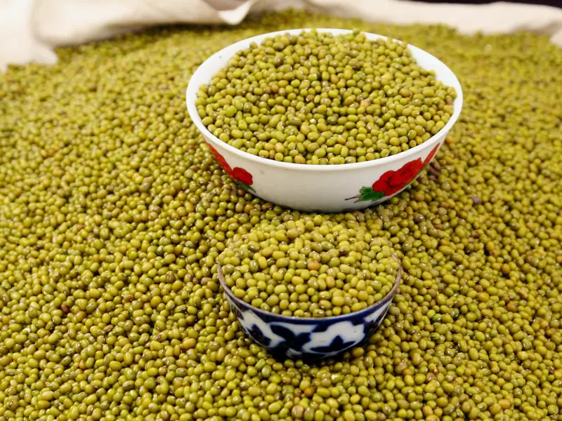 Grüne Mungobohnen werden in zwei traditionell verzierten Schalen auf einem belebten Basar in Usbekistan angeboten.
