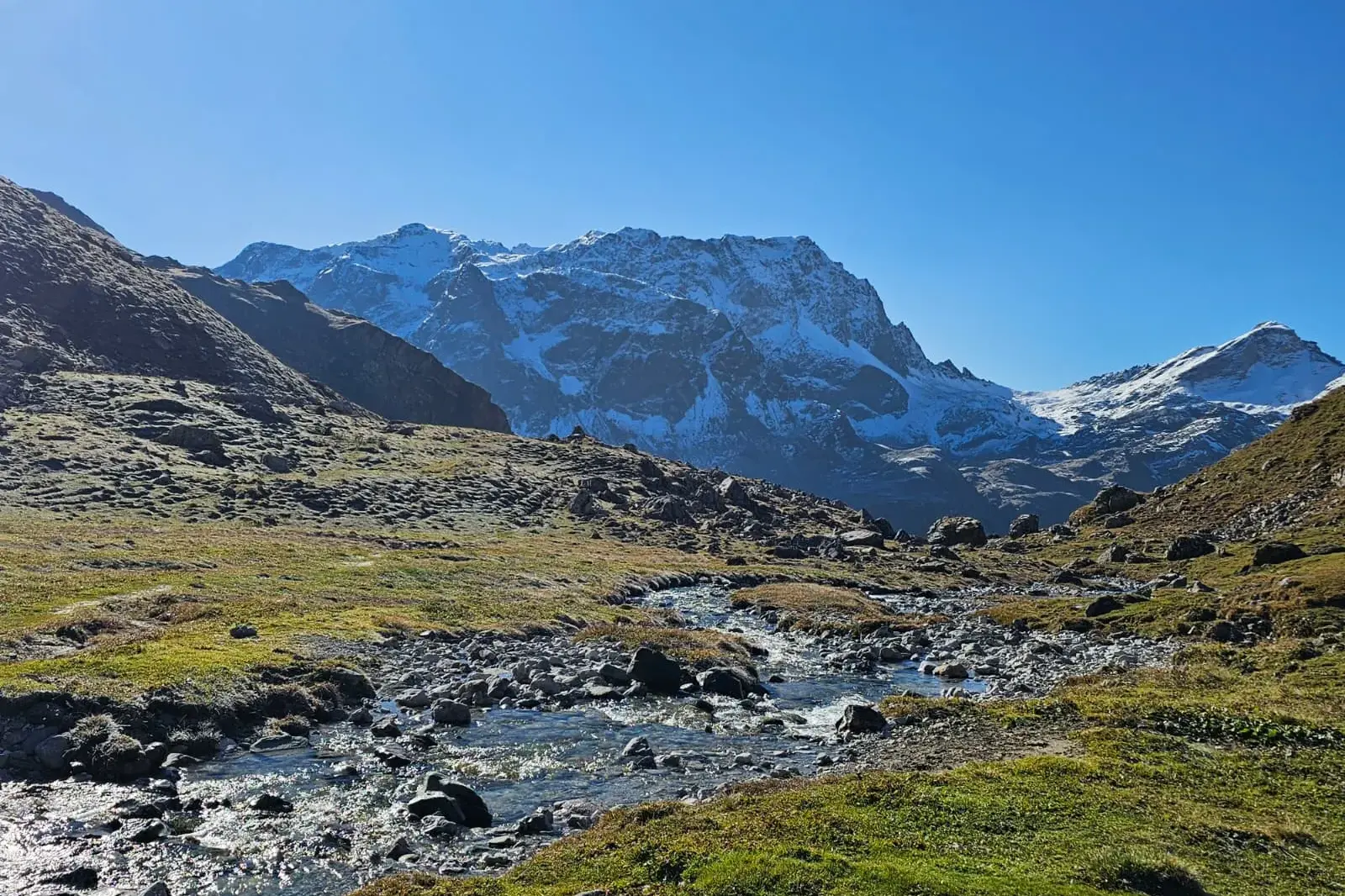 Klarer Bergbach auf einer Wanderung in den Graubündner Alpen mit Blick auf schneebedeckte Gipfel bei Bivio.