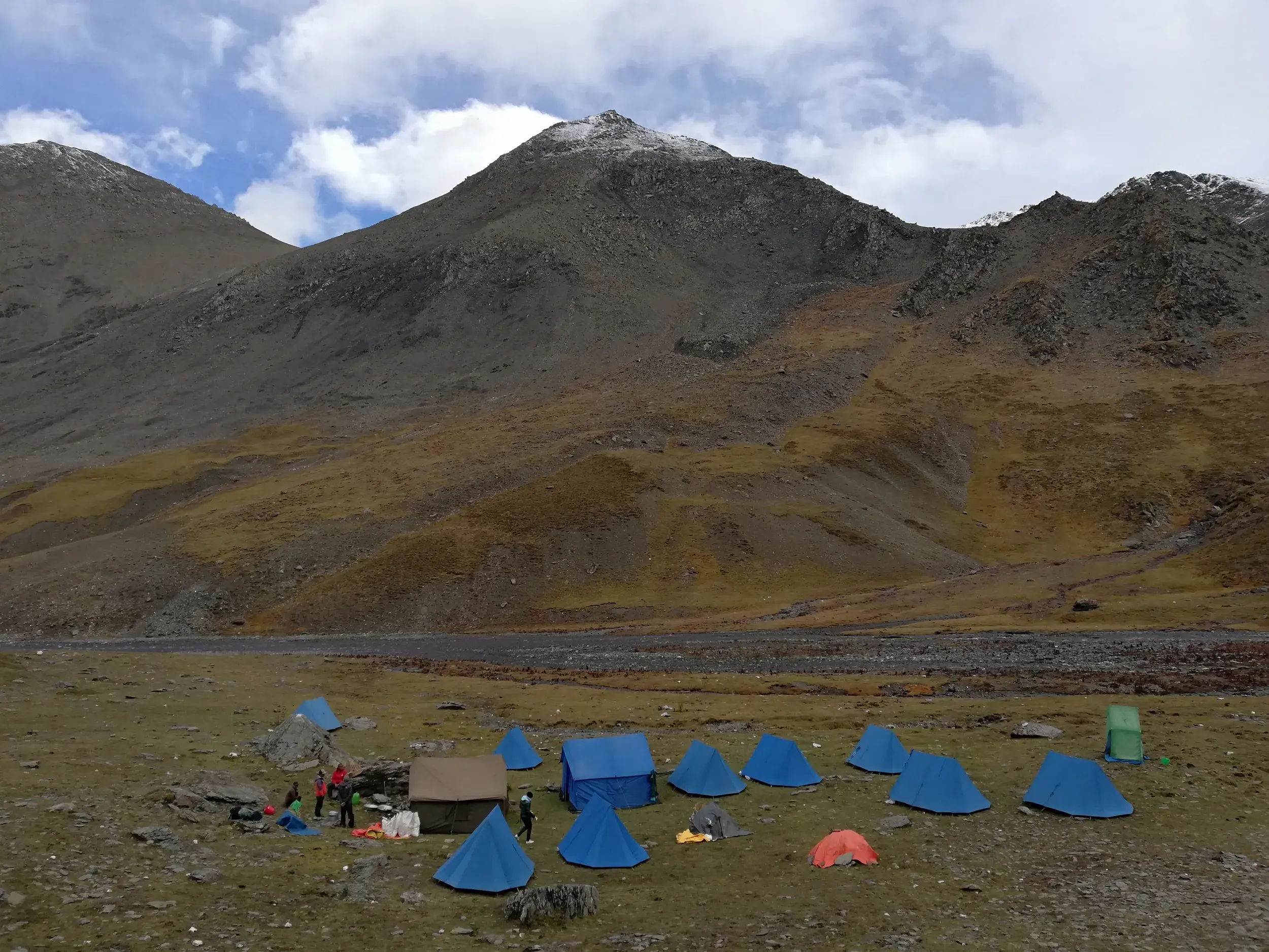 Zeltlager einer Trekkinggruppe mit blauen Zelten in einem weiten Tal vor der kargen Bergkulisse des Dolpo in Nepal.