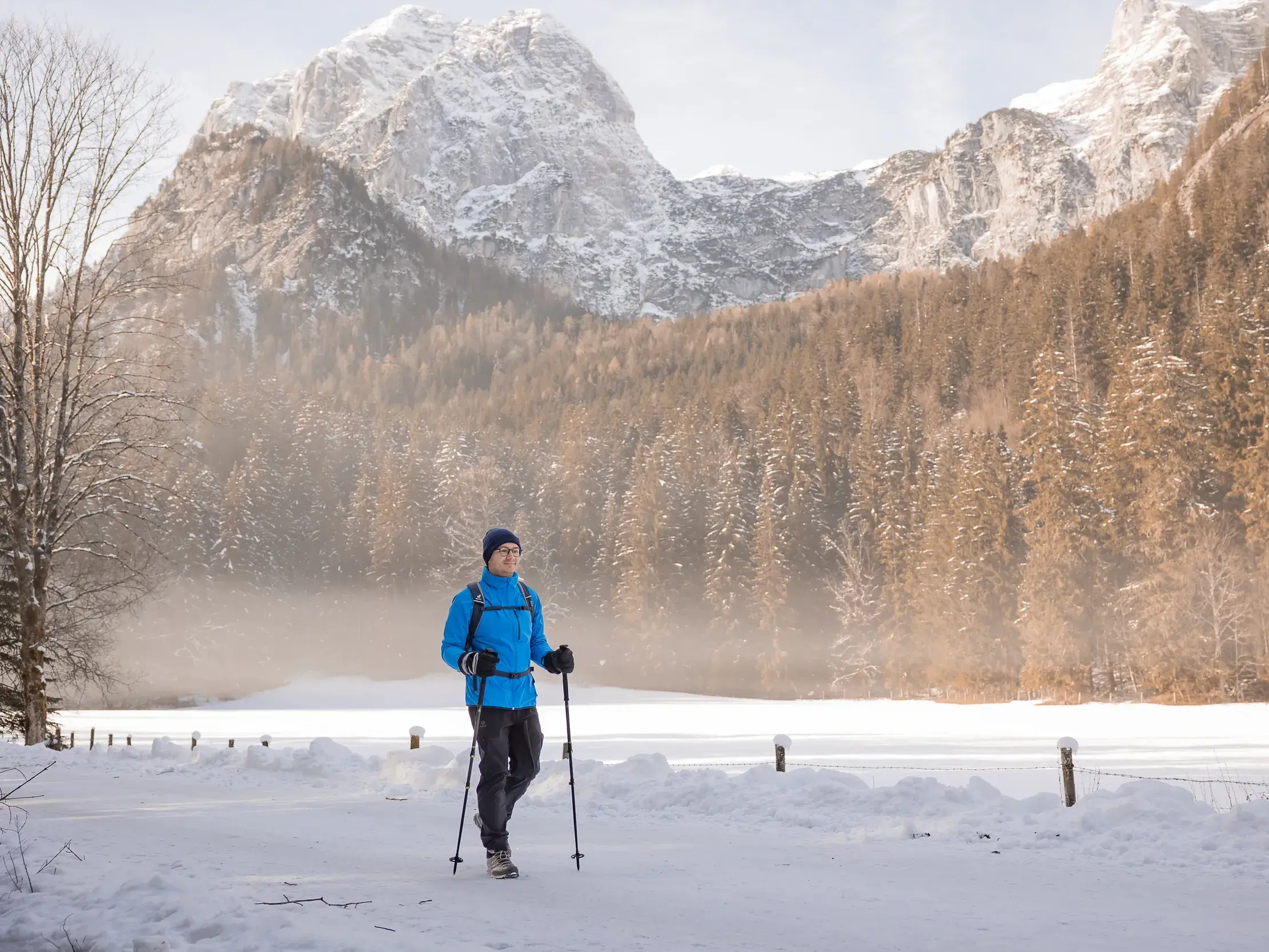 Ein Wanderer in blauer Jacke wandert durch den Schnee vor der eindrucksvollen Kulisse der Ramsauer Dolomiten.