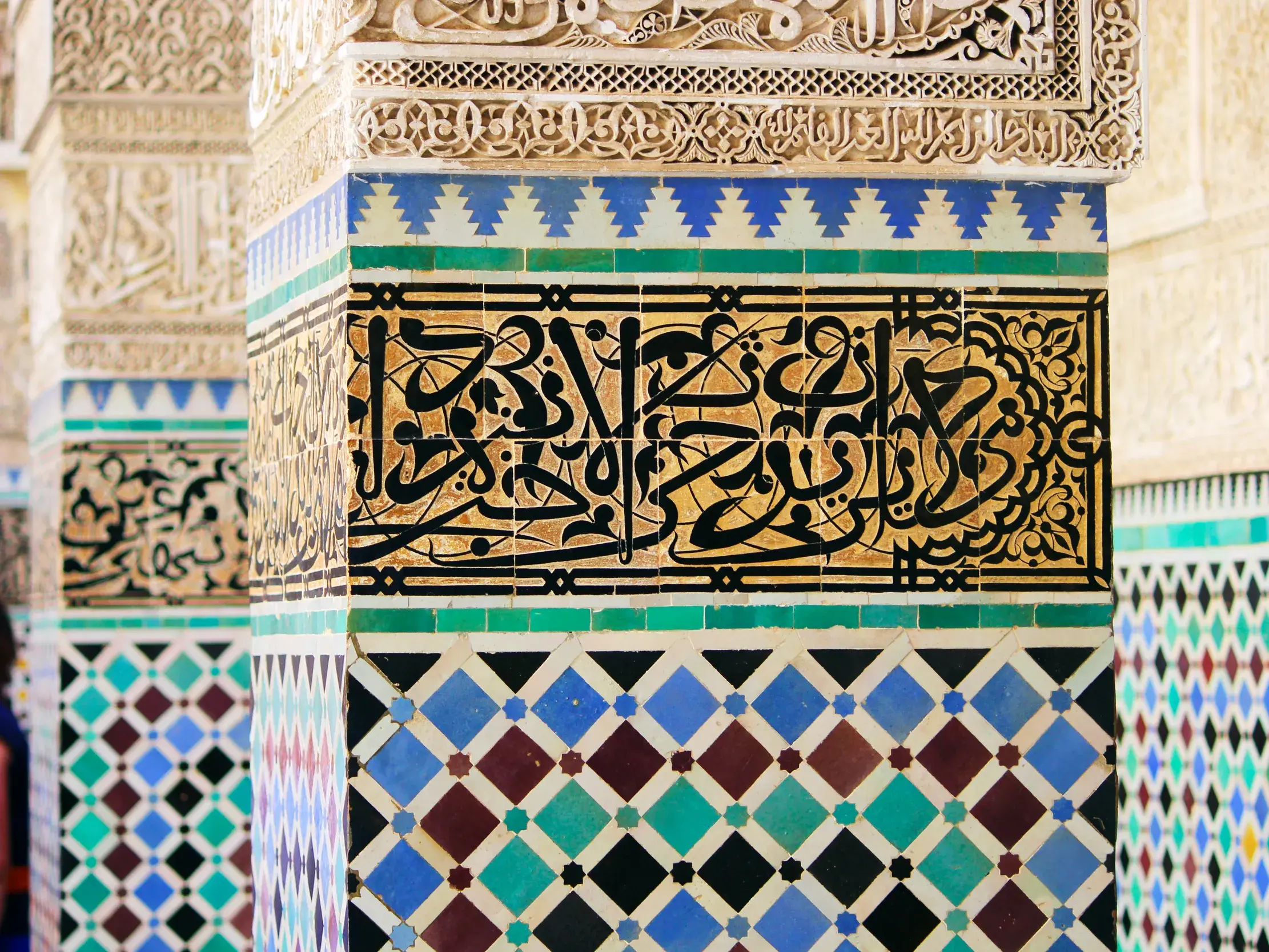 Nahaufnahme einer kunstvollen Säule mit marokkanischen Mosaiken, bunten Zellige-Fliesen und arabischer Kalligraphie.